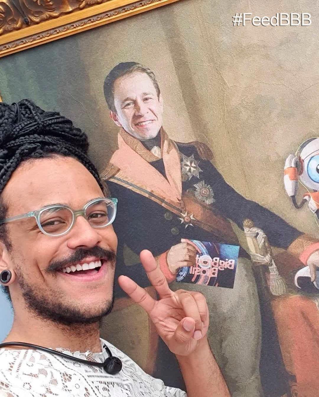 Joao Luiz poses with a painting of Thiago Levert in the leader's room that day "BBB 101 Day" - clone / Instagram