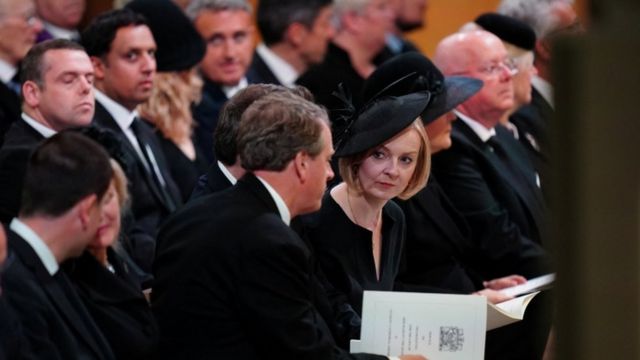 Liz Truss sitting surrounded by other people dressed in black