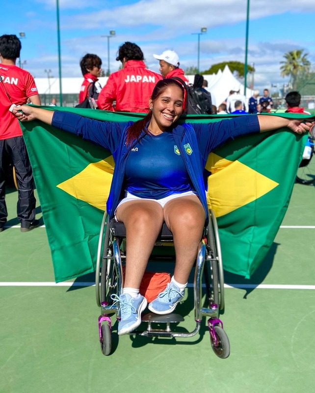 Jade is in a wheelchair holding a Brazilian flag and smiling for a photo