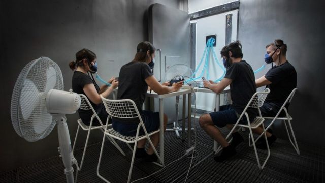 Four people sitting around a table in matching clothes with oxygen masks in their mouths